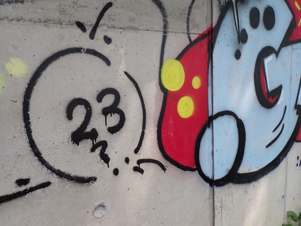 Links in unterbrochenem Kreis eine "23", rechts ein hellgraues "G", darunter teilweise eine rote Fläche mit gelben Punkten. .