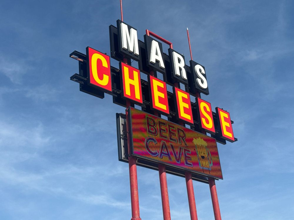The road sign of “Mars Cheese Castle” with an LED board showing “Beer Cave”. 