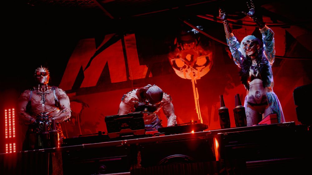 Cyberpunk 2077 screenshot of 3 Maelstromers on stage at the Totentanz. The one on the left is standing with his arms in front of him, clasping his hands together. The one in the middle is working the dj equipment. The one on the right is waving her hands in the air. 
The background is red with the letters "M L S T R M" with an upside down skull between the S and the T. The M L R M letters and skull are painted in red while the S and T are painted in black.