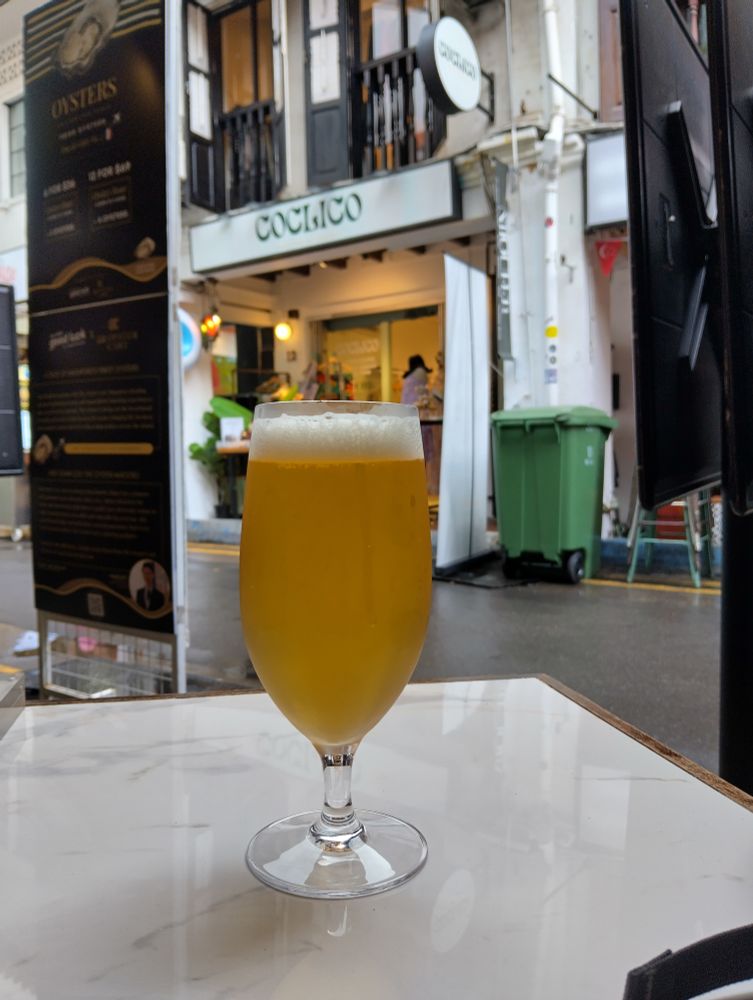 A stemmed glass of beer on a marble table. Street scene in the background.