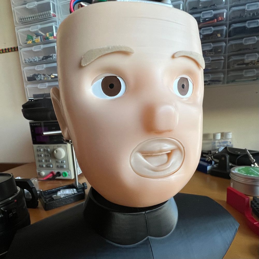 A hard plastic doll's head on a cluttered desk. The mouth is clearly a separate element, and the eyebrows look a bit fishy, but the overall impression is of a clean and keen perky little fellow.