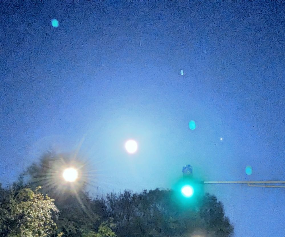 Grün leuchtende Verkehrsampel vor einem wolkenlosen Sternenhimmel mit Vollmond.