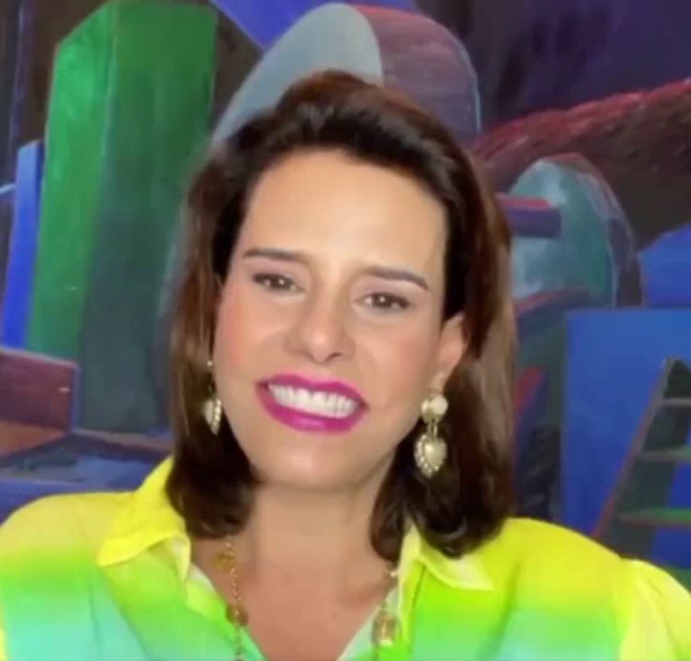 a woman in a yellow shirt and earrings is smiling in front of a colorful background .