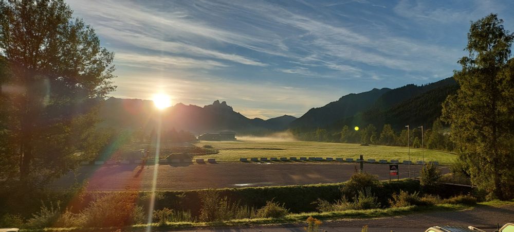 Sonnenaufgang zwischen zwei Bergen davor ein flaches, leicht in Nebel gelegenes Tal 