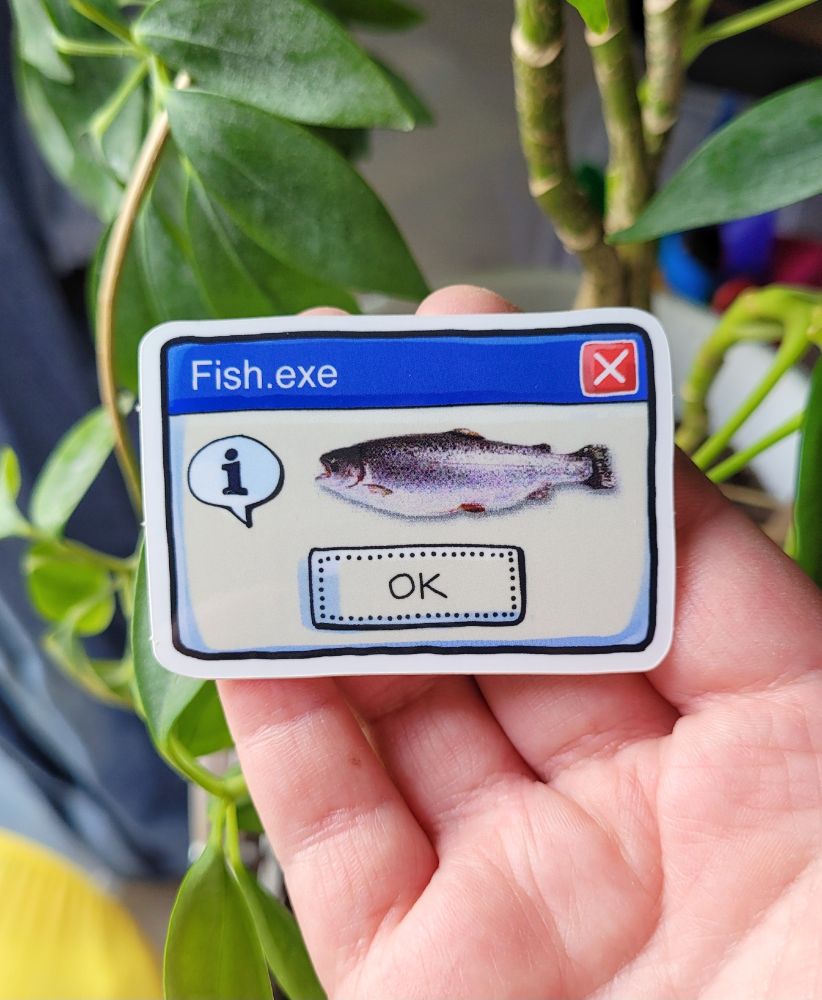 Photo of my hand holding a sticker. The design is a hand-drawn microsoft pop-up window. The top blue border has left centered text in it that reads "Fish.exe", on the right side is a red square with an "x" in it. On the grey part of the window is a fish at the center. On the left side of the fish is a speech bubble with an exclamation mark. The button bottom center says "OK".
