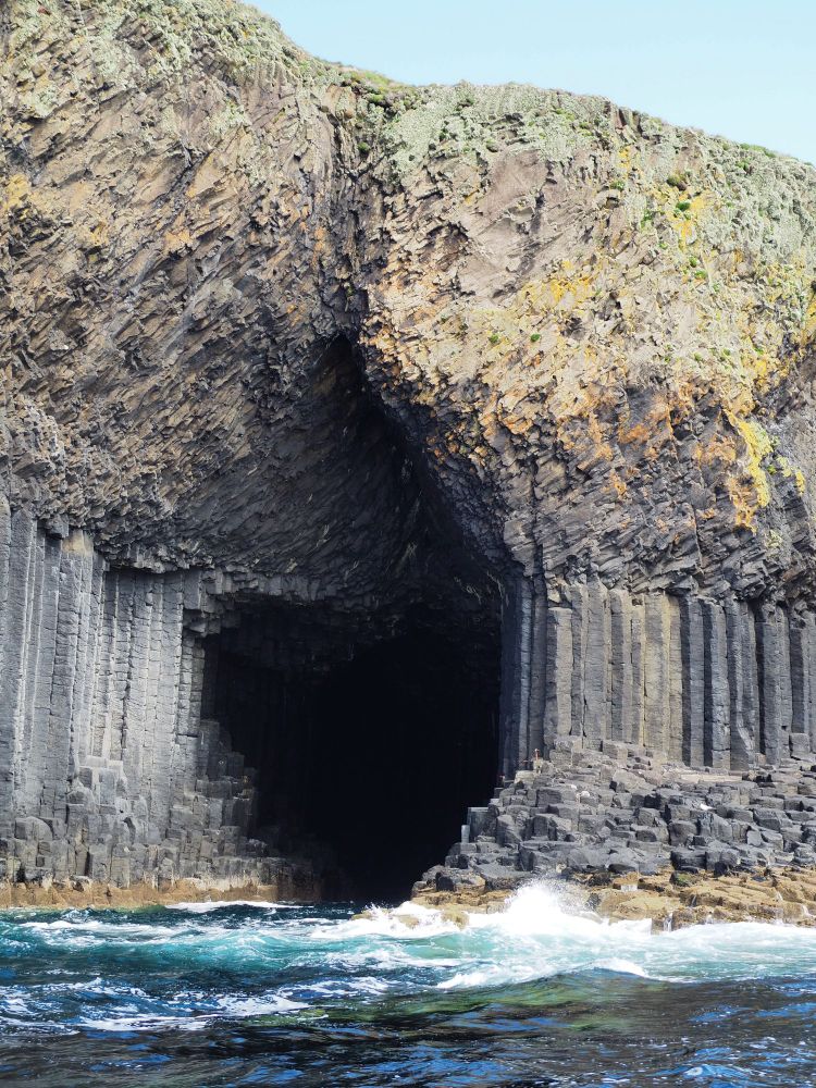 The mouth of a deep sea-cave extending into the columnar basalt cliff.