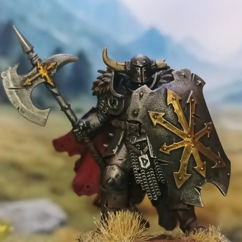 A chaos warrior in a steel armor with a gold trim, wearing a red cape and wielding a shield and halberd