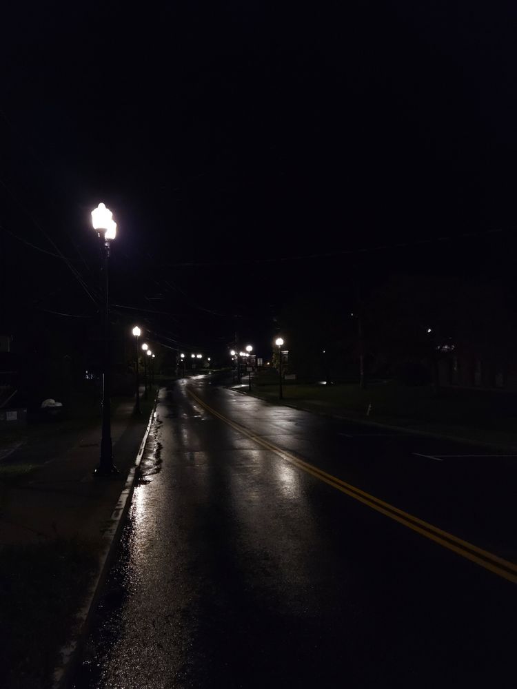 A road at night, after some rain, the street lamps reflect on the pavement
