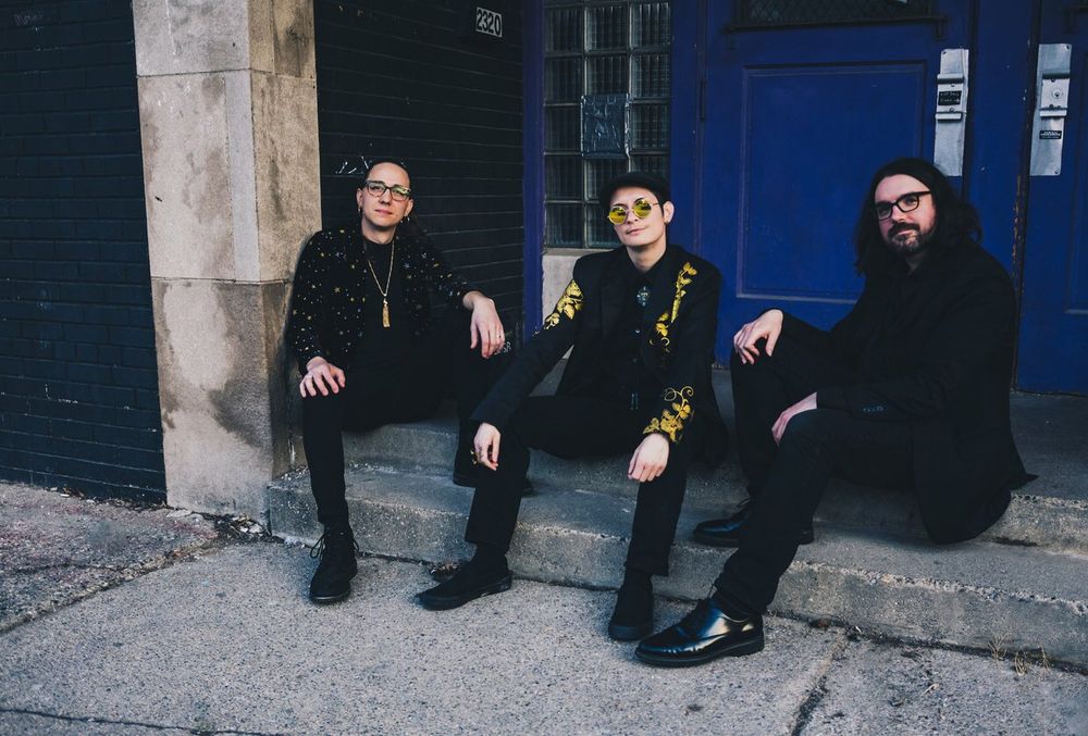 Three people wearing black sit on some stone steps leading up to a large door