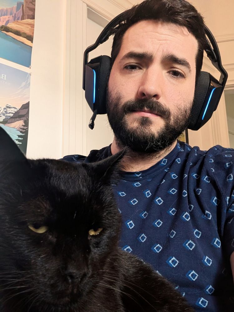 A man wearing headphones with a black cat in his lap