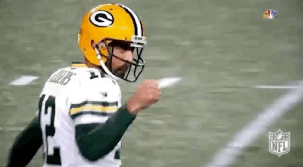 a green bay packers football player wearing a yellow helmet is pointing to the sideline .