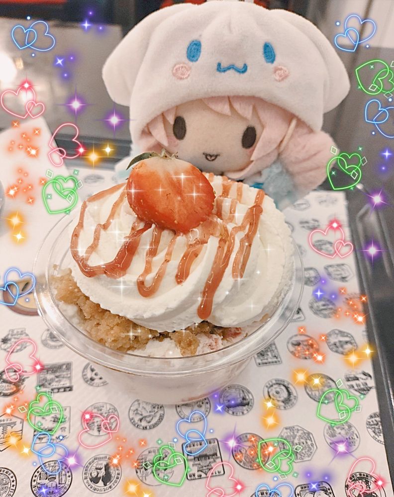 An Akiyama Mizuki nui plushie in front of a strawberry parfait. The picture is edited with a bunch of colorful hearts and sparkles around.