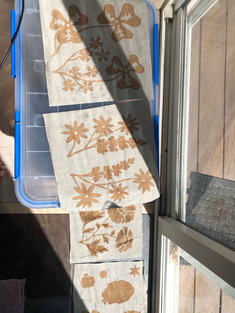 Pieces of beige linen with a rust colored iron mordant paste painted on in floral patterns, waiting to be dyed in coffee