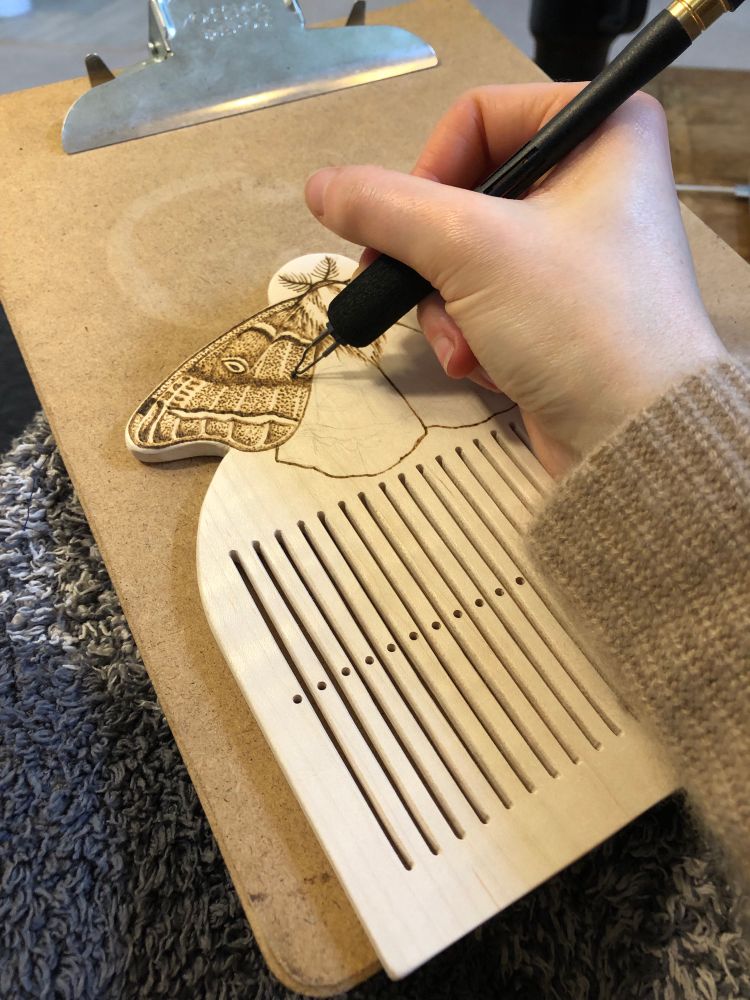 A work in progress of a moth being wood burnt onto a maple rigid heddle