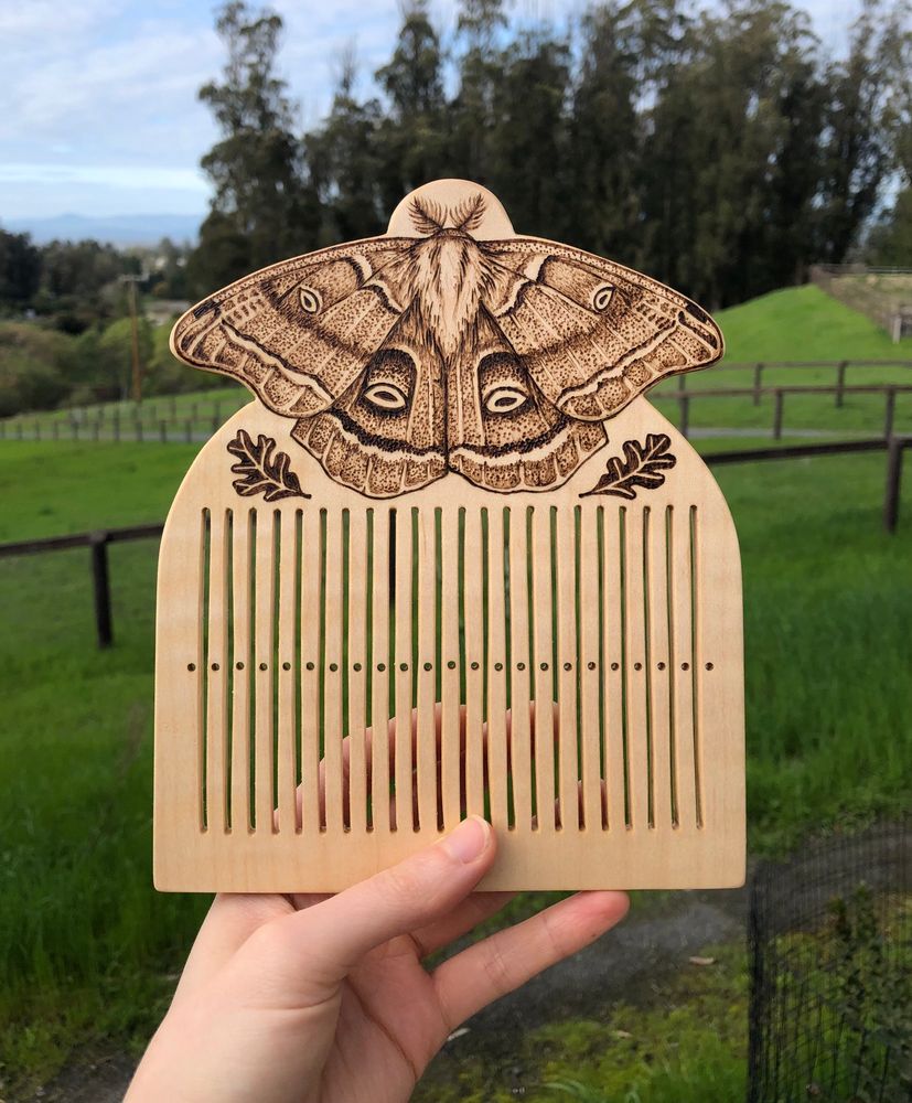 A handmade wooden rigid heddle featuring a polyphemus moth and oak leaves, with 45-thread capacity
