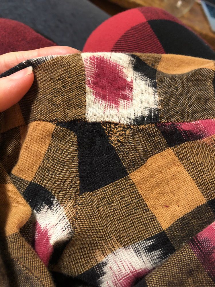 A hand sewn crotch seam repair on a pair of yellow and black gingham pants. The stitching is color matched to the gingham