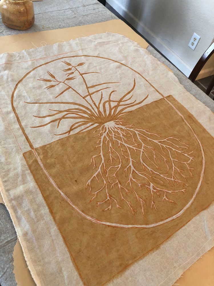 An image painted onto linen using an orange iron mordant paste. The image is of a California oat grass plant, above and below ground