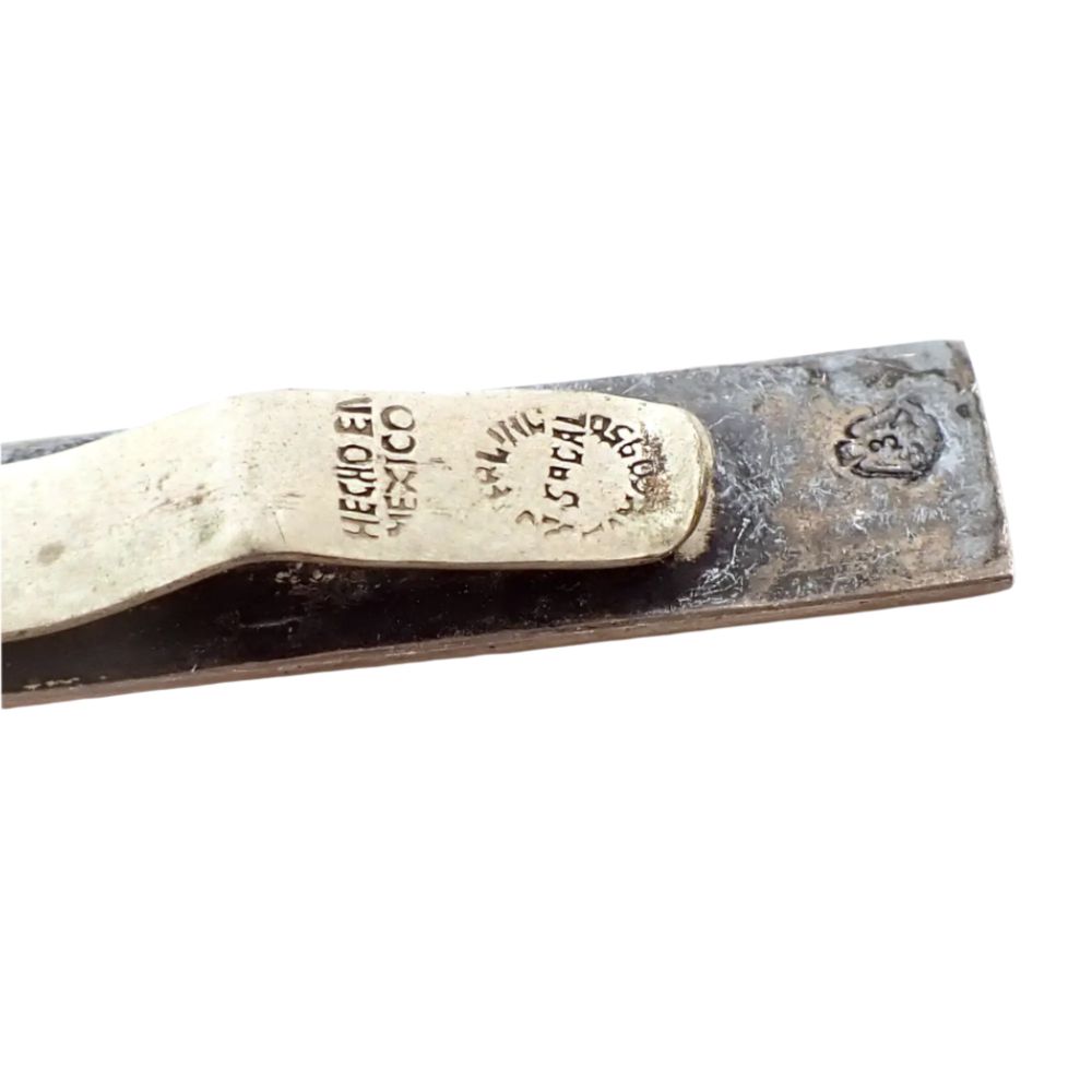 Enlarged close up view of the backside end of the tie bar where the markings are. The clasp part has Hecho en Mexico, Sterling, Taxco 950, and what looks to be V Sacal. The bottom part of the tie bar itself has an eagle marking with a 3 inside of it.