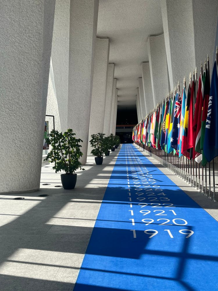 A blue carpet with years on and a line of flags inside a grey building.
