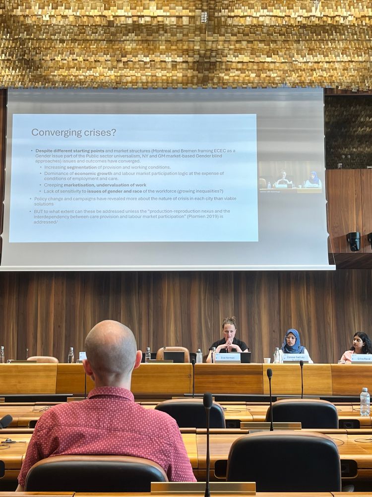 Three women on a panel presenting to a room of attendees with a PowerPoint presentation behind.