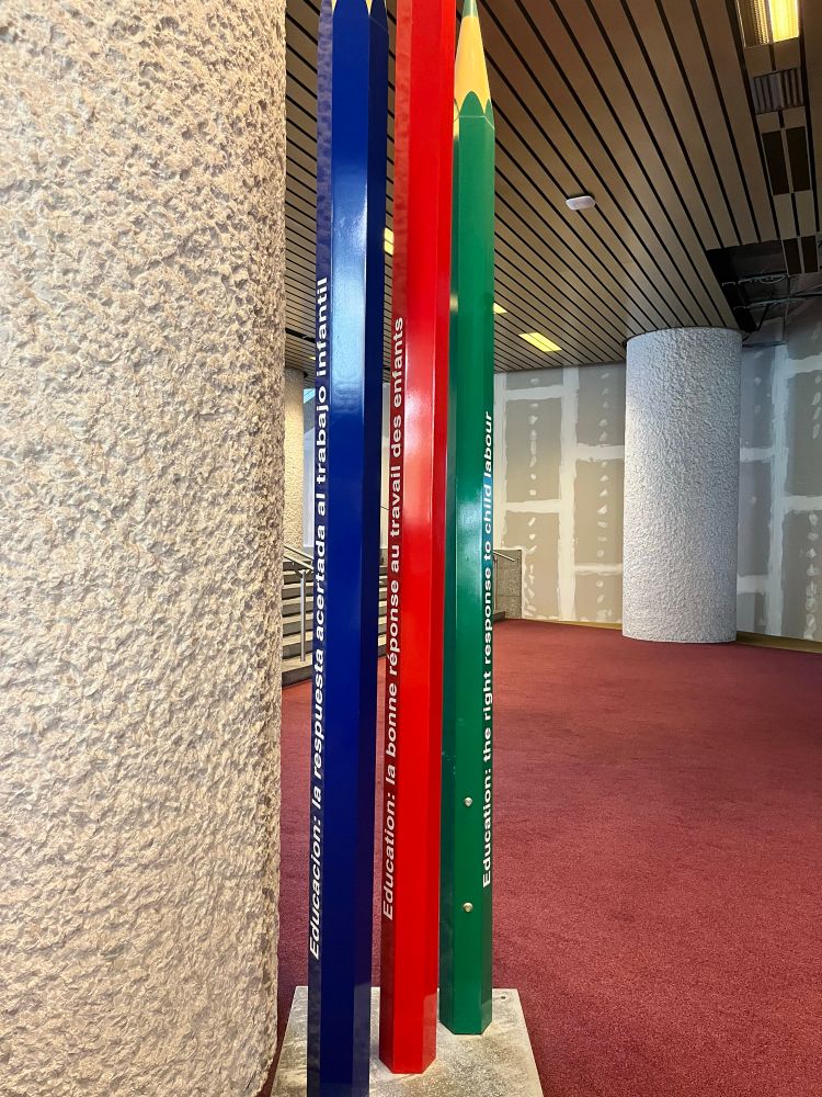 3 giant pencils next to a concrete wall on a red carpet 