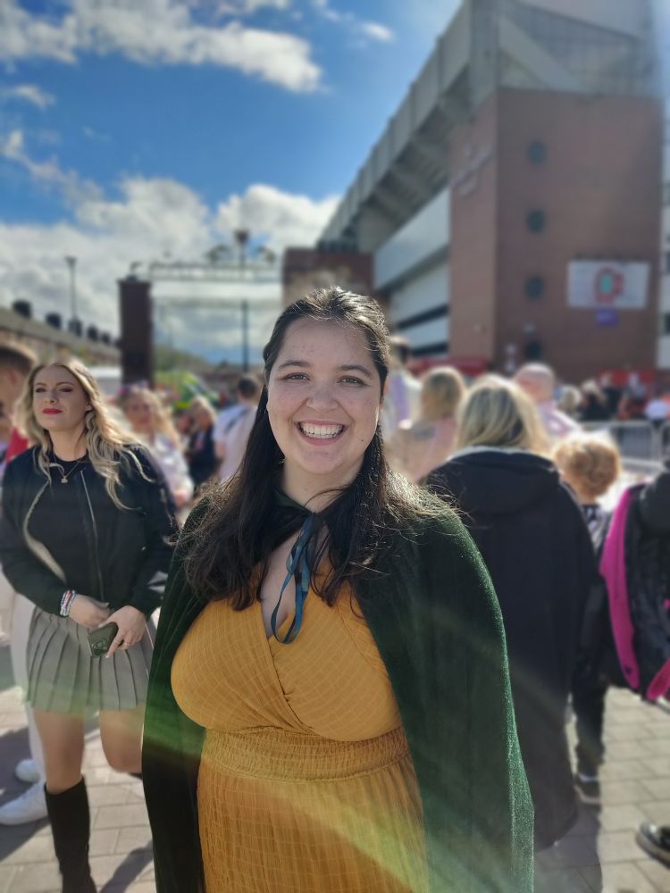 A girl outside of Liverpool stadium (Anfield) in a yellow dress and greencap