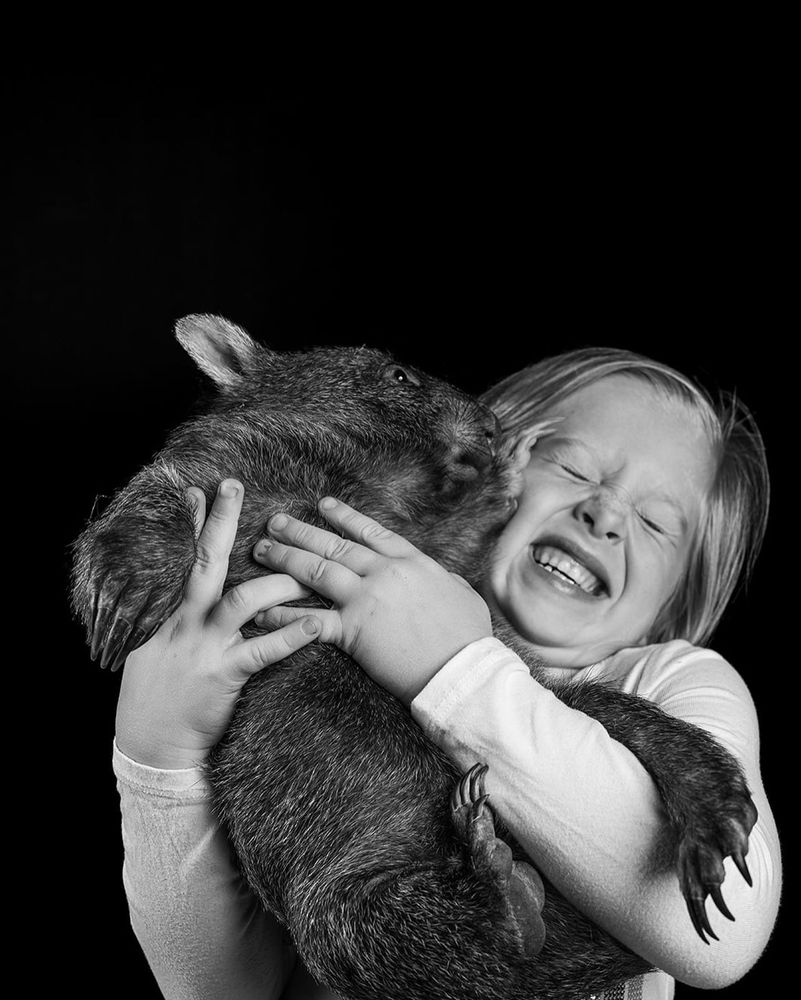 child laughing while hugging a fluffy wombat in black and white (credit: Josh Neille)