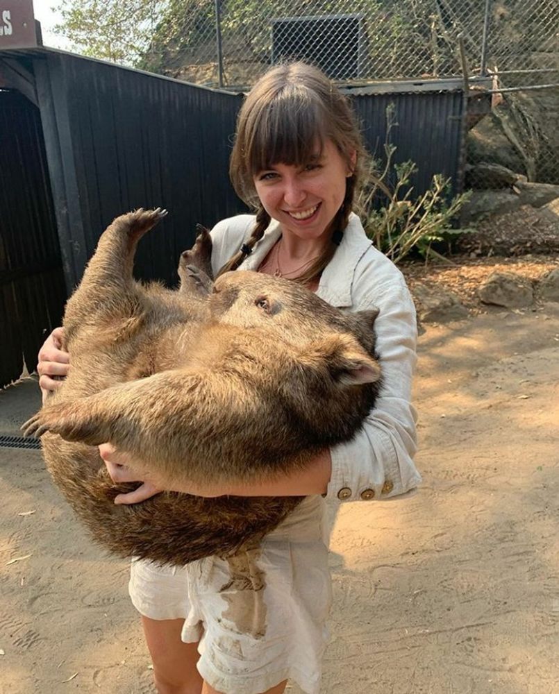woman holding a large wombat outdoors smiling in a casual outfit