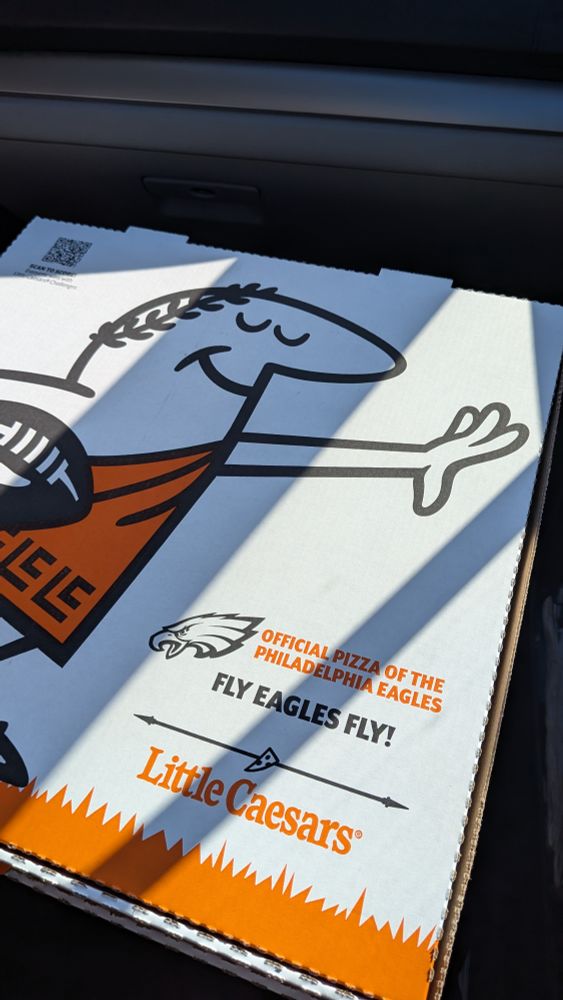 the top of a little Caesar's pizza box. the little Caesar is carrying a footbal. below him text reads "official pizza of the Philadelphia eagles. fly eagles fly". there is an eagles logo next to the text. 