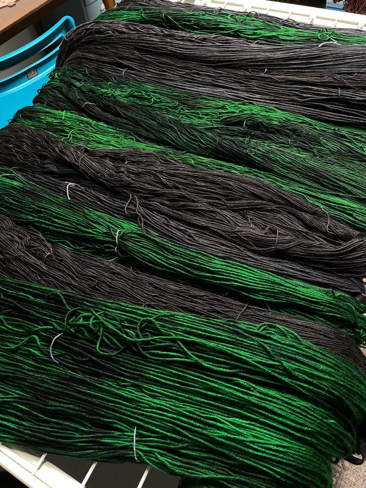 Emerald and black indie dyed yarn damp on a drying rack. Colors are Ex Libris Fibers The Green Lion and Aniline Black shown on yak sock, sock, and dk bases.