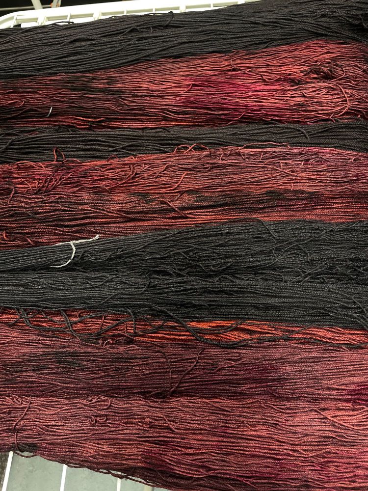 black and red indie dyed yarn on a drying rack. The colors are Mina Murray and Aniline Black.