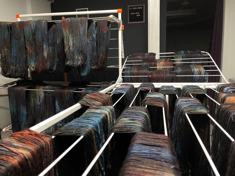 Dark variegated earth tone indie dyed yarn hangs to dry in a dark basement workspace