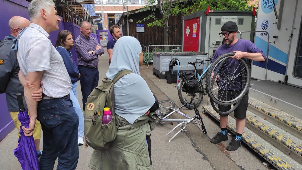 A man from A Different Gear holding up a bicycle tyre in front of a group of Grantham Centre scholars and supervisors. He is demonstrating how to remove the inner tube of the tyre. 