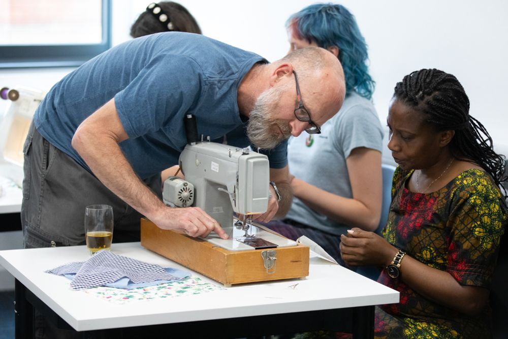 A man from Reyt.Repair leaning over a sewing machine to show a Grantham Scholar how to use it.
