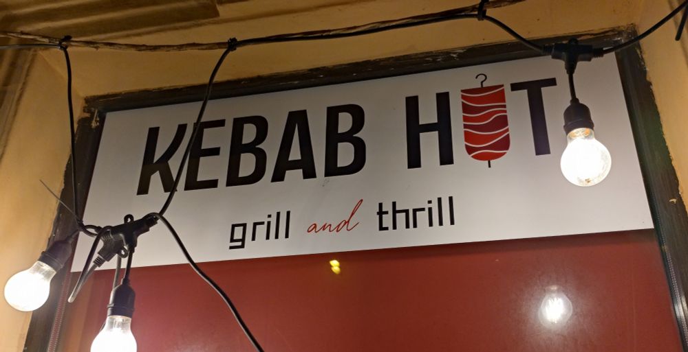A signboard reading

KEBAB HUT
grill and thrill

The U is drawn like a stylised shawarma skewer, so I'm not sure if it is 'hut', 'hot', or 'hit'
