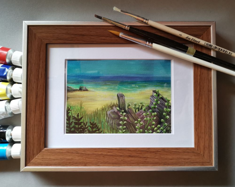 Zu sehen ist ein Foto eines Gouachbildes hinter Glas. Links sieht man die Farbtuben die verwendet wurden und rechts oben die 3 Pinsel die ebenfalls beim Entstehen dabei waren.

Bild: Gouachebild auf dem eine Strandlandschaft zu erkennen ist. Der Betrachter ( also man selbst) sieht direkt auf der rechten Seite einen Holzkarren der seine besten Jahre bereits hinter sich hat und sich Pflanzen daran festhalten.Links zwei Felsen direkt am Strand .