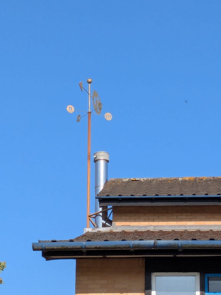 A mysterious weathervane sculpture on top of a building on University of York's campus againsta a blue sky.