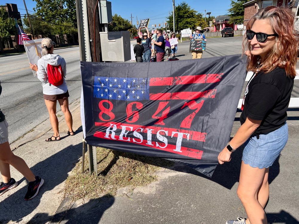 Woman holding the side of a black flag with white stars in a blue field on the left top, four red stripes separated by the numbers 