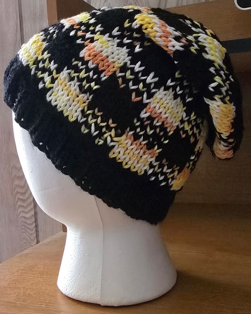 A slouchy knit hat with a plaid pattern in yellow, white, and orange on a black background. 