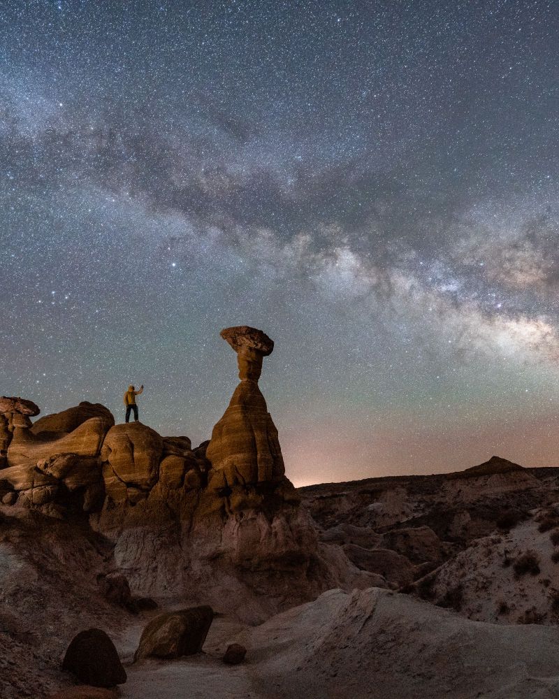 A man standing on the Toadstool Hoodoos under the milky way