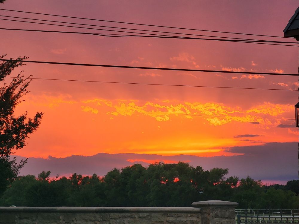 Fiery sunset over a treeline. Brilliant oranges blend vividly into a deep purple. 