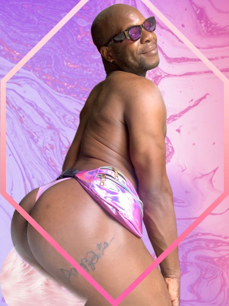 I am slightly crouching from behind, I am wearing brown sunglasses with purple lenses and a purple vinyl fanny pack, the decor is purple, I am wearing a bubble gum pink thong.