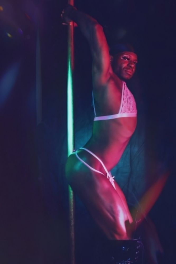 I am arched, I hold the pole dance bar from above, I am in profile and I am looking at the lens from the side.