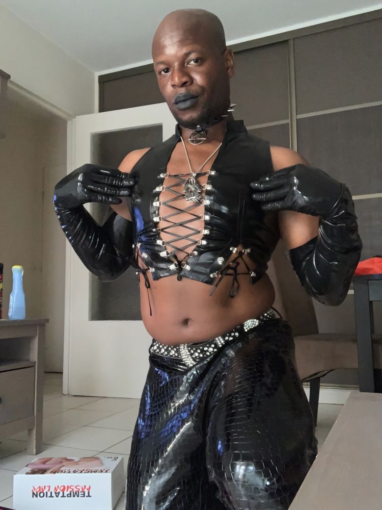 I'm on my knees, dressed in black, I'm wearing New Rock boots, black crocodile pants, a leather top with low-cut straps, latex opera gloves, a choker necklace with a metal pentagram pendant and black lipstick.