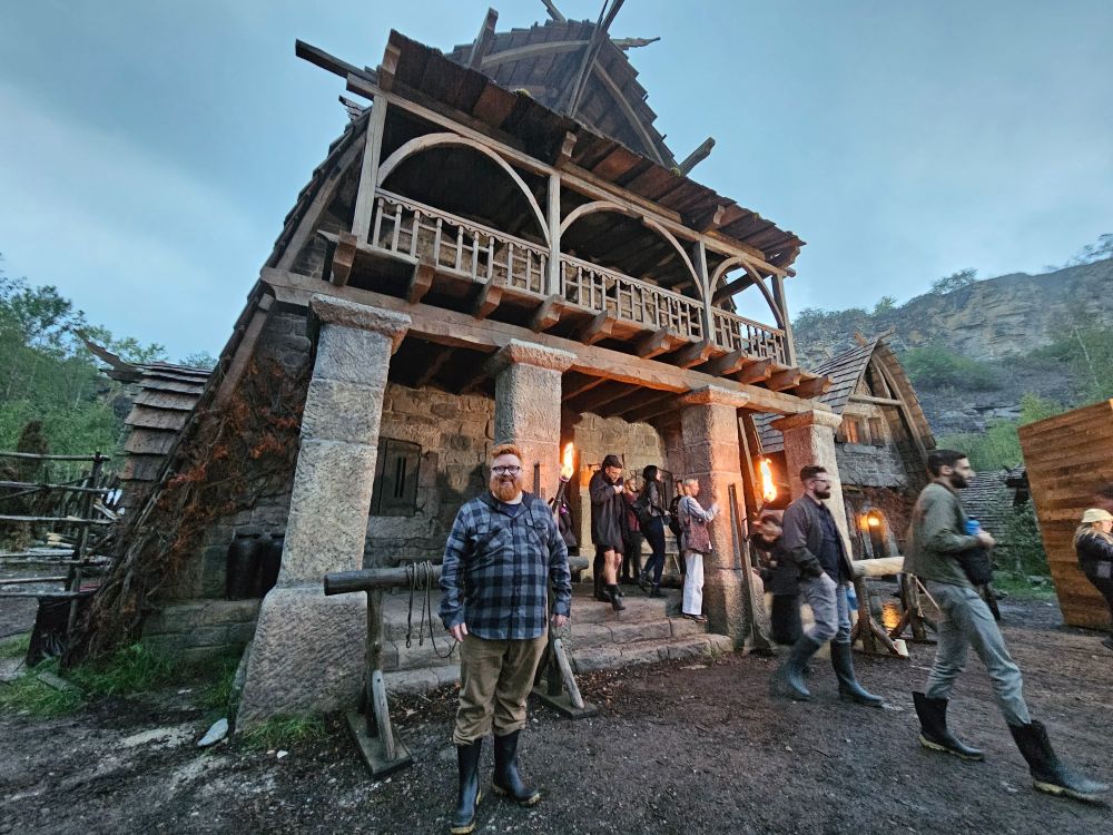Me standing in front of the Winespring Inn set in Prague in the Two Rivers village during my visit there in 2023. Other people from the media are walking by as I pose awkwardly in front of the Inn.