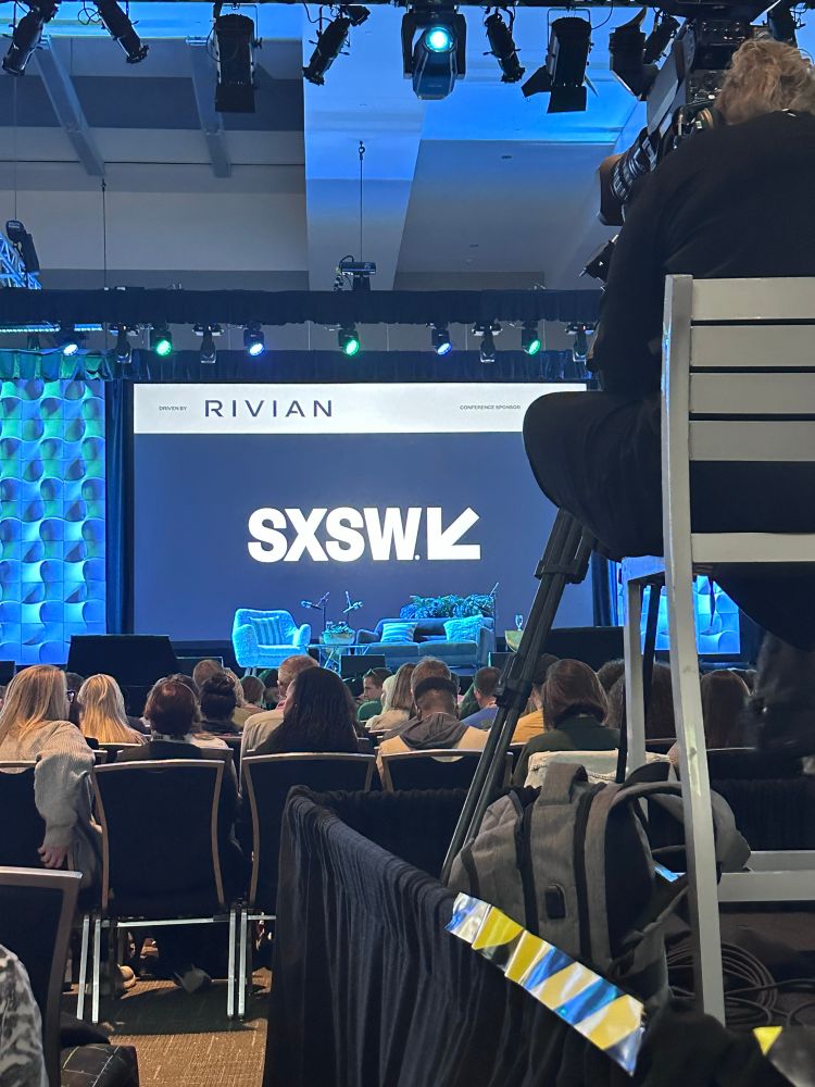 SXSW main stage. A couch and chair on the stage with microphones for podcasting. The SXSW logo is projected behind the stage