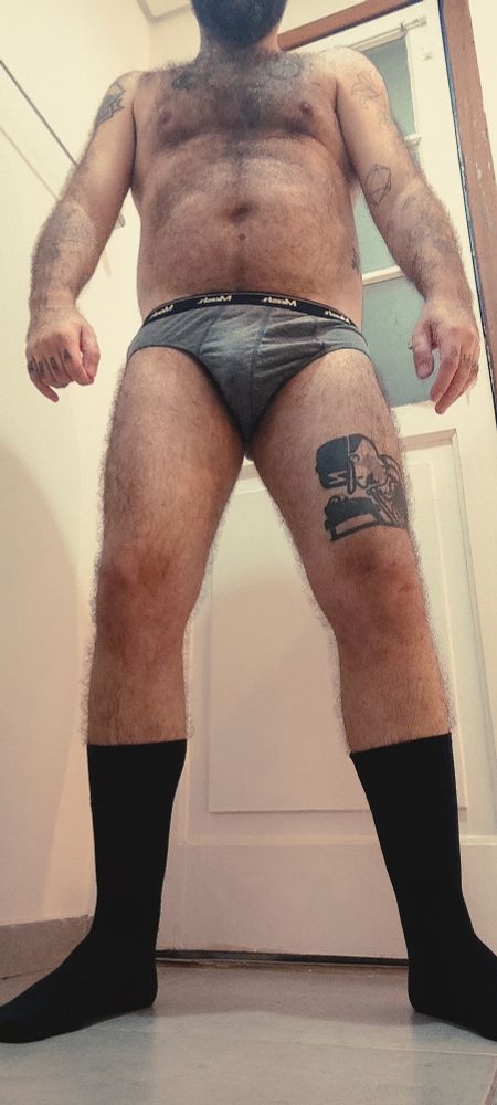 Eu de pé, visto de baixo, vestindo apenas uma cueca cinza e meias pretas até o meio das canelas