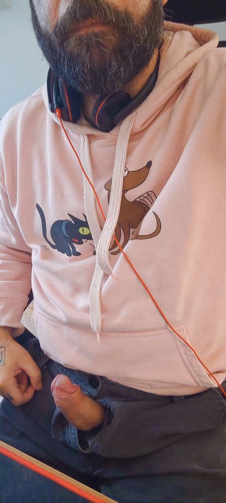 Me wearing a pink hoodie and black jean shorts. I'm sitting on my office chair and my hard, thick, uncut penis is showing through the fly.