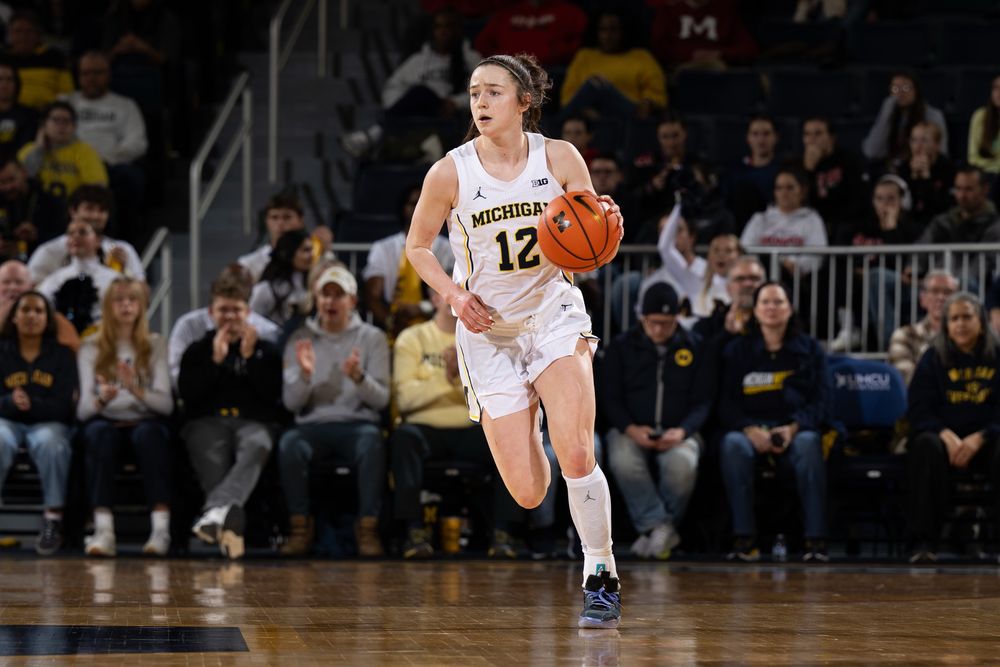 Michigan Wolverines freshman shooting guard Syla Swords in a white uniform with number 12 running with a basketball in her left hand during a game.