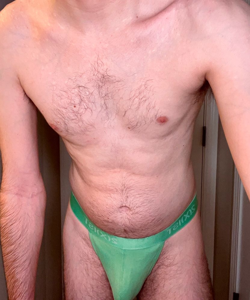 leaning into the camera wearing only a green thong with full pouch suggesting a hard cock is tucked inside
